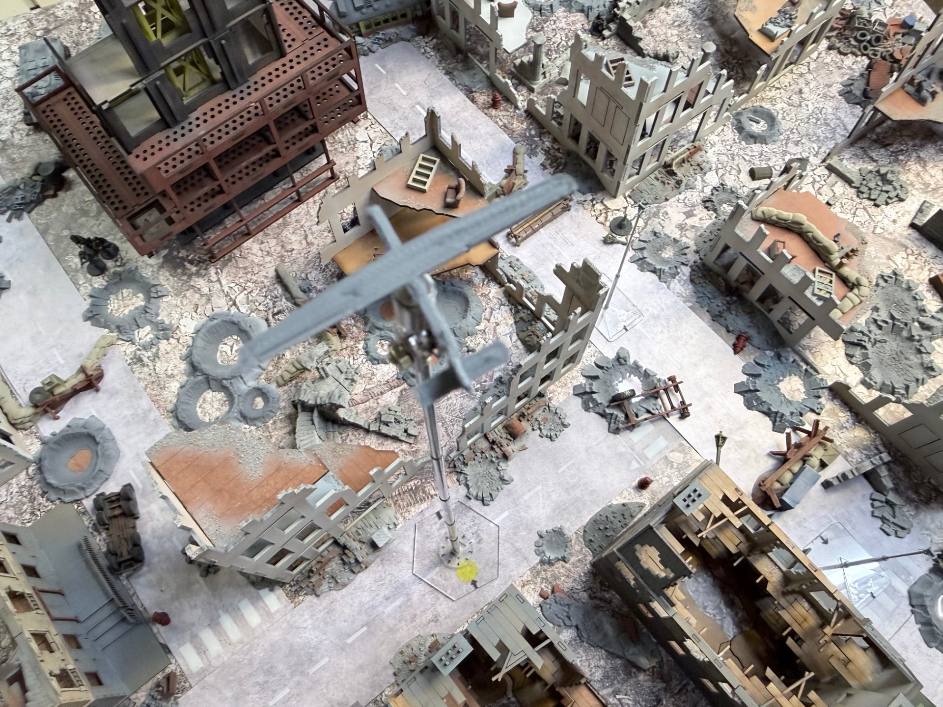 A fixed-wing recon UAV on a tall flight stand above a cratered ruined intersection