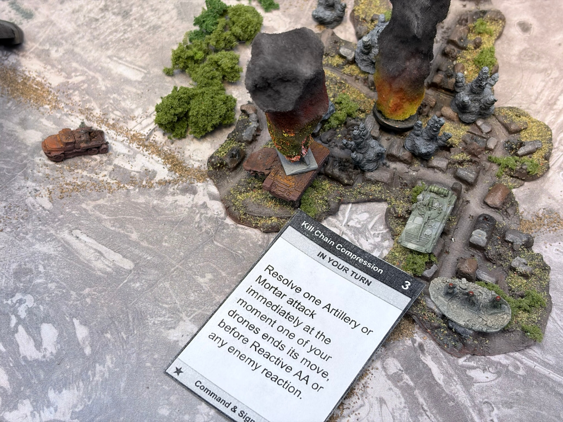 Explosions among vehicles and infantry on a rubble base with a Kill Chain Compression card in the foreground