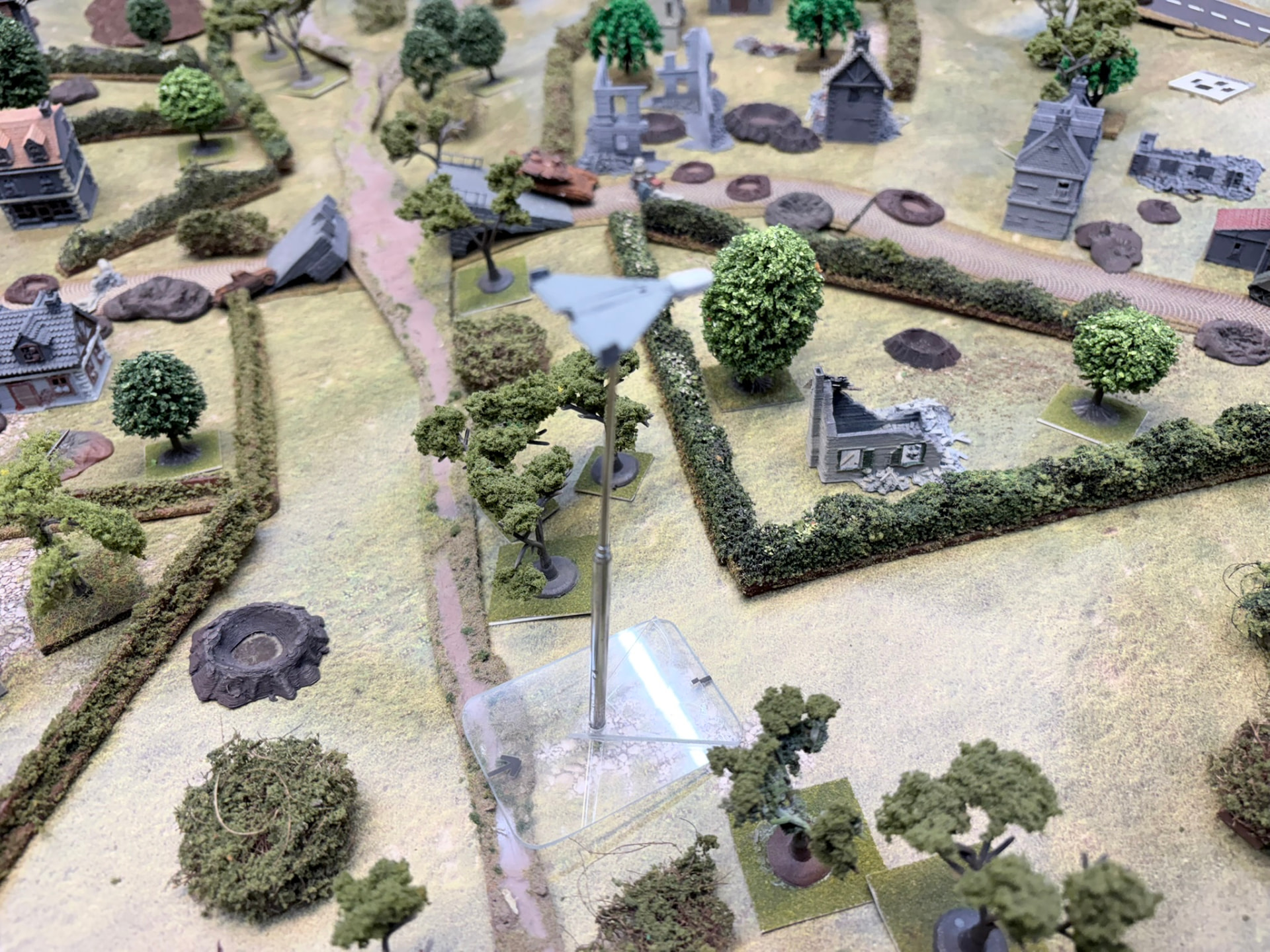 A delta-wing one-way attack drone on a tall flight stand above a rural table of fields, roads and ruins