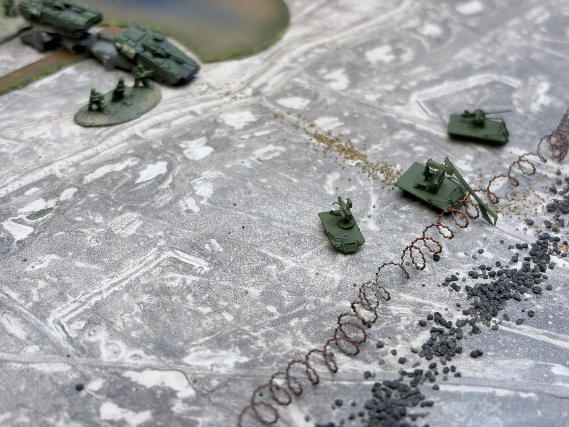 Tracked ground drones advancing on a concertina wire obstacle with armour and infantry behind