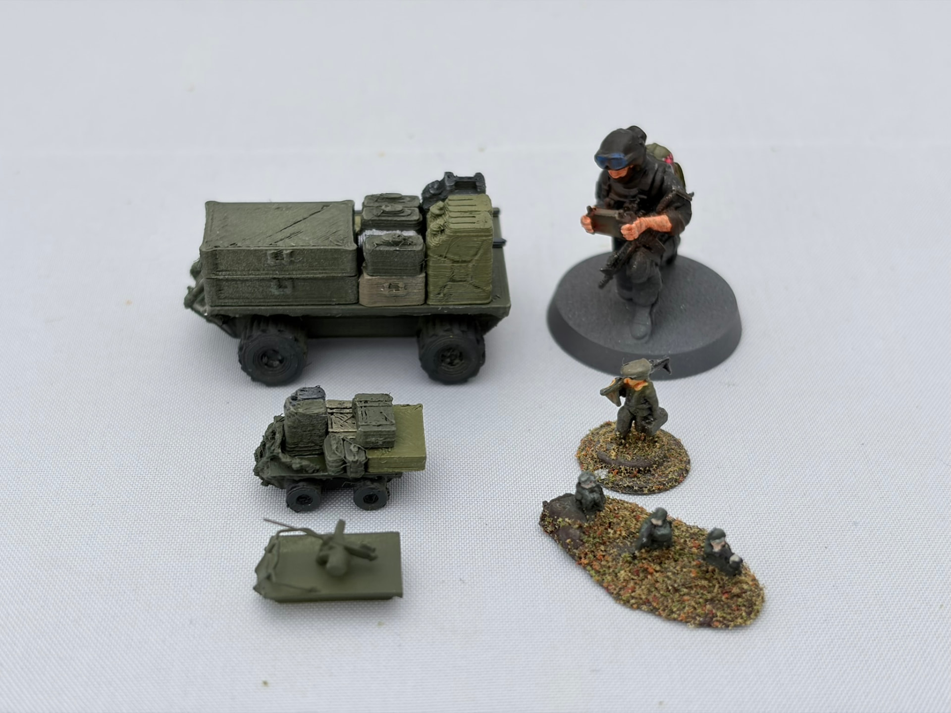 Printed logistics ground drones shown beside miniature figures in three different scales