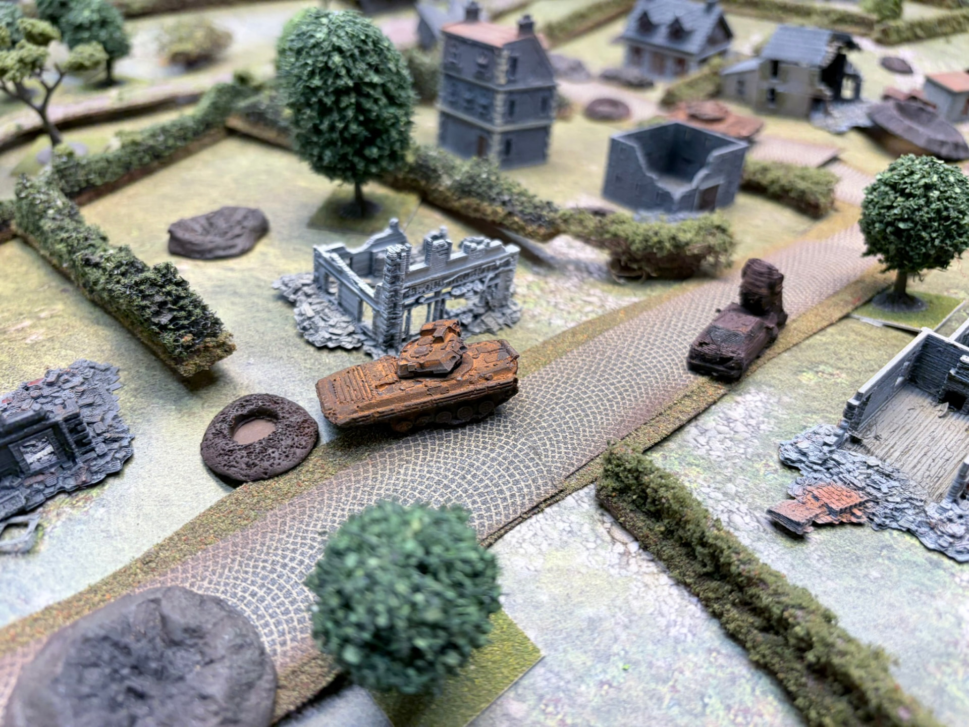 A burnt-out tracked IFV and shell craters on a cobbled village lane beside ruined buildings