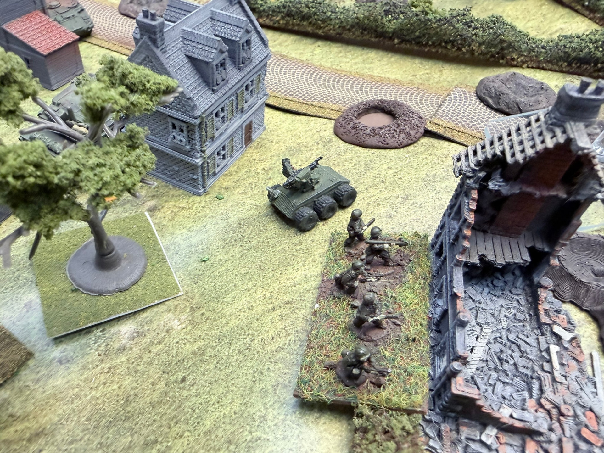 An infantry squad on a flocked base moving up a village street with an armed UGV gun platform behind