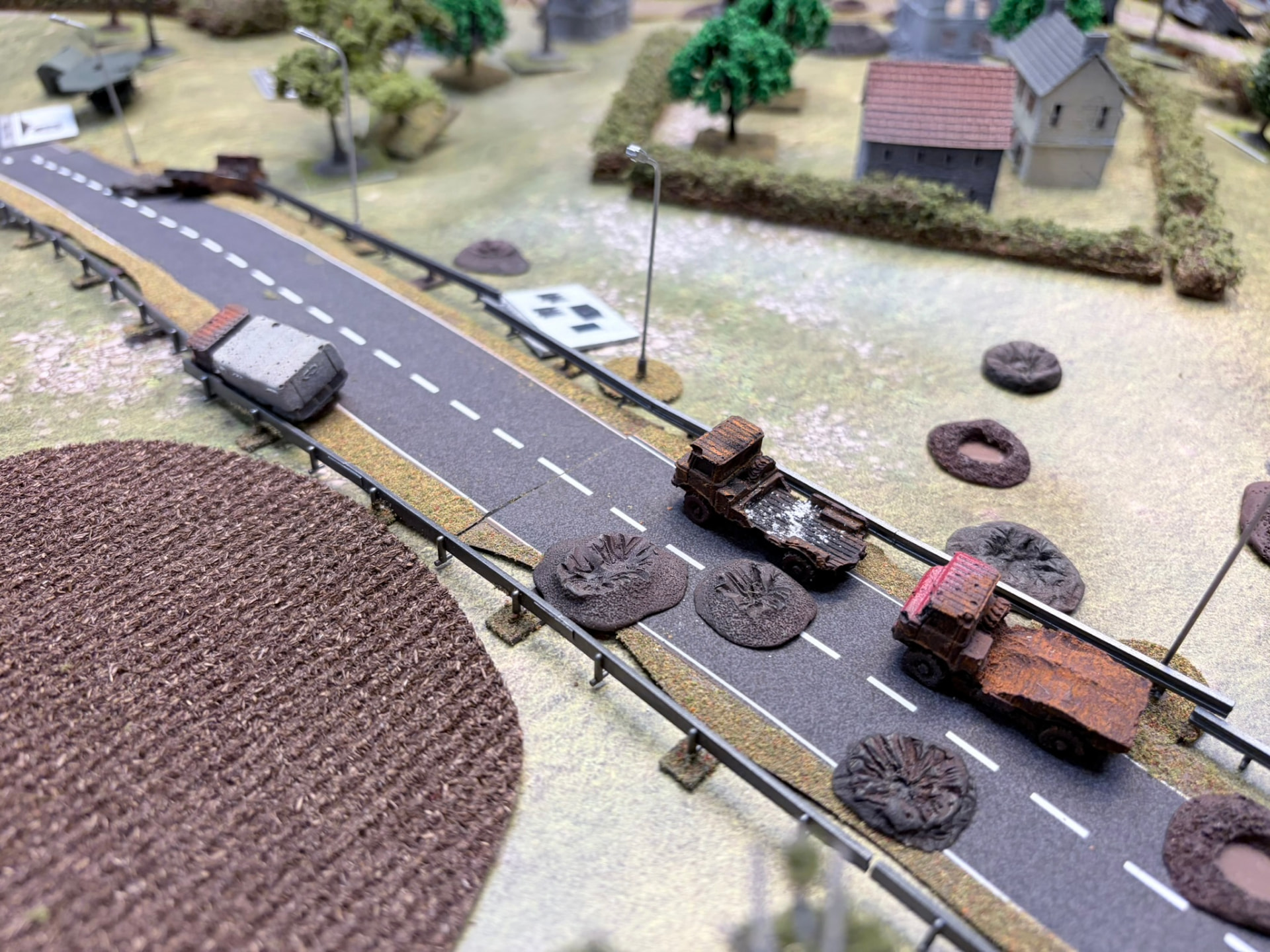 Wrecked trucks and blast craters blocking a paved highway between hedgerows