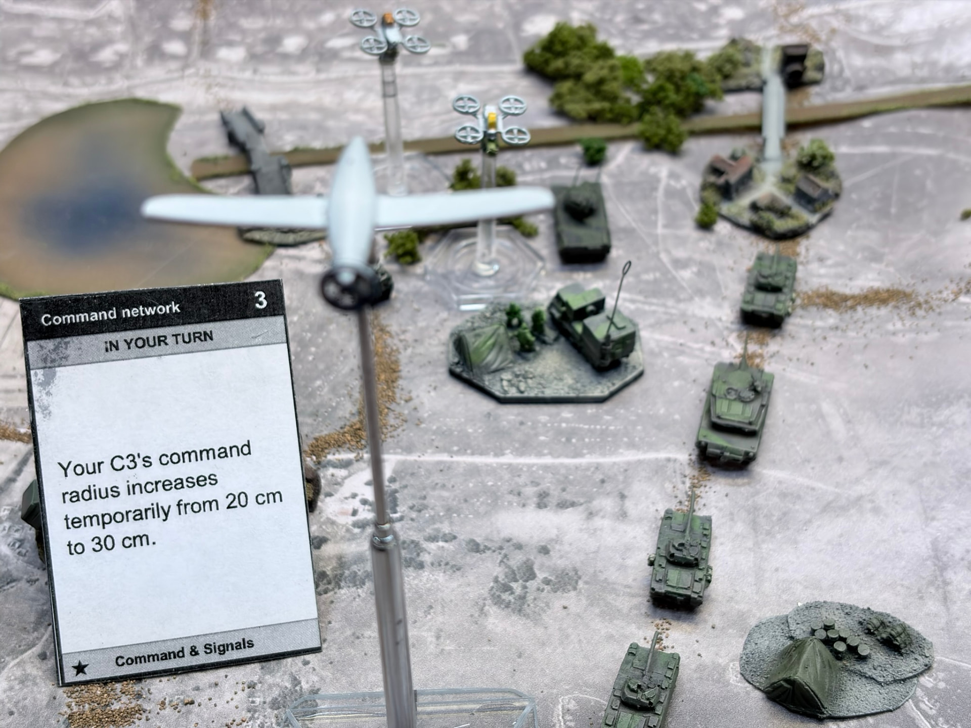 Recon drones on flight stands above an armour column with a Command network card in the foreground
