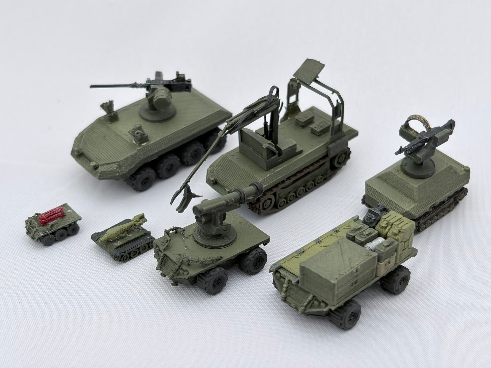 Seven printed ground drones in olive green, wheeled and tracked versions